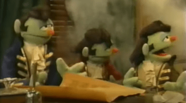 Three Elvis-style Muppets in Revolution-era coats gathered around a table