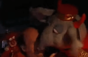 Pepe and Seymour are on either side of Jason Alexander's shoulders in their bellhop outfits, but Pepe has angel wings and Seymour has devil horns.