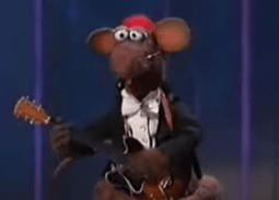 Rizzo in a tuxedo and red hat, playing an electric guitar